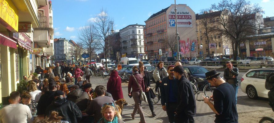 Belebter Bürgersteig mit Außengastronomie, Fußgängern und Radfahrern